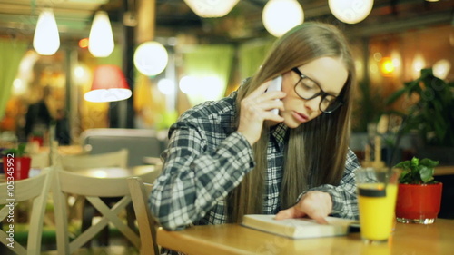 Girl in glasses and plaid shirt talking on cellphone while sitting in the cafe
 photo