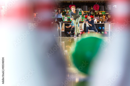 Group of friends on an active night out, bowling in a bowling alley, seen from the point of view of the pins