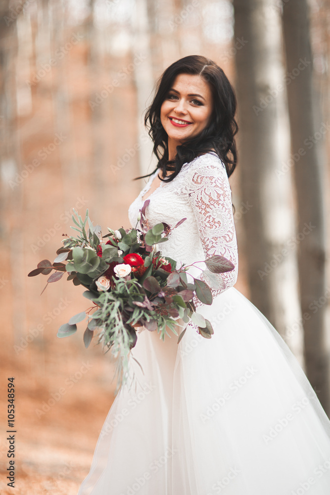 Gorgeous brunette bride in elegant dress holding bouquet posing near forest and lake Gorgeous brunette bride in elegant dress holding bouquet posing near forest and lake