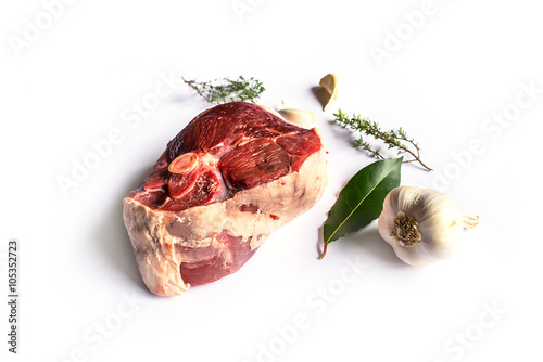 beautiful raw slice of an organic leg of lamb meat with garlic, fresh bay laurel and thyme on a white background with blur background