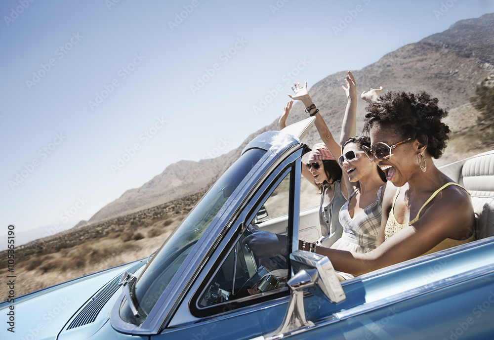© Mint Images - Three young people in a pale blue convertible car, driving on the open road across a flat dry plain, © Mint Images - Three young people in a pale blue convertible car, driving on the open road across a flat dry plain,