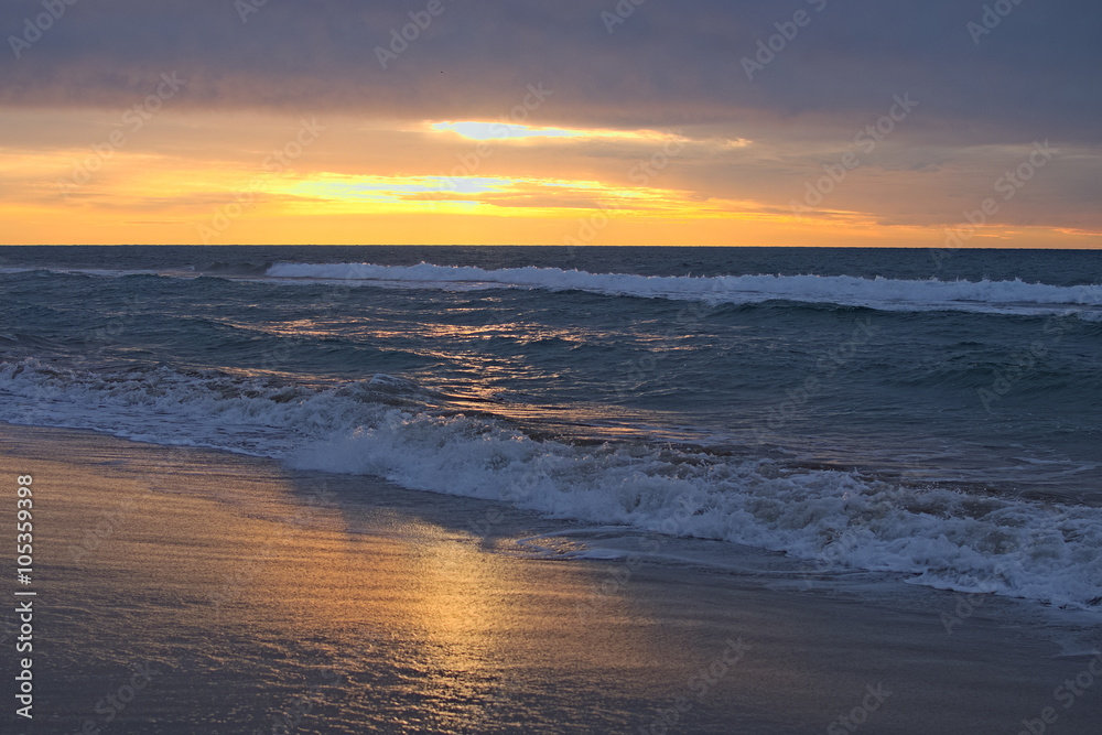 Fabulous sunrise on the beach. The sun breaks through storm clouds and reflected in the water and on the sand. Waves rolled on shore