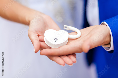 White wedding lock in the form of heart in the hands of the bride and groom. Wedding theme, symbol of love, newlyweds