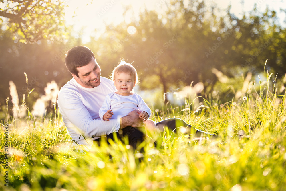 Father holding his little son, sitting on the grass Father holding his little son, sitting on the grass