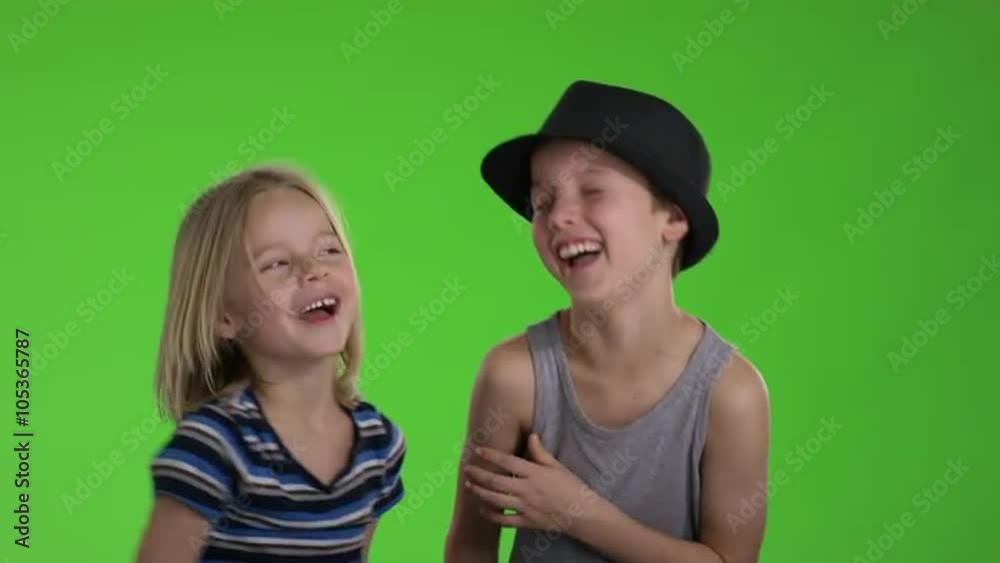 Child whispers a joke to another child in front of greenscreen Child whispers a joke to another child in front of greenscreen