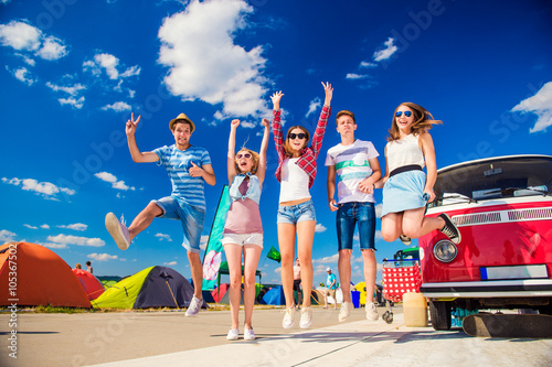 Teenagers at summer festival jumping by vintage red campervan photo