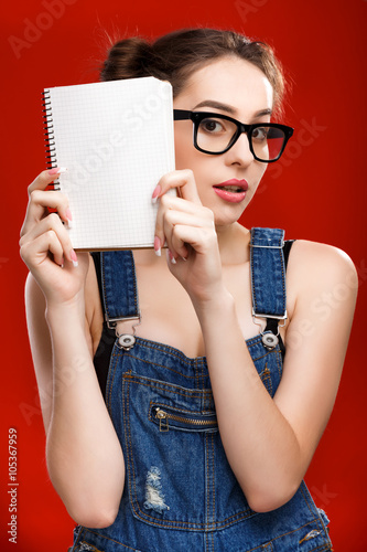 Charming girl holding notebook near her face in studio