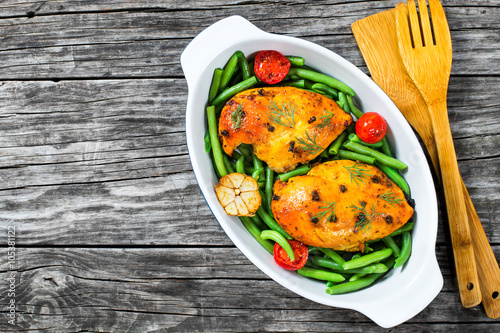 Chicken breast with green bean, garlic and tomatoes in the baking dish decorated with fennel leaves, view from above