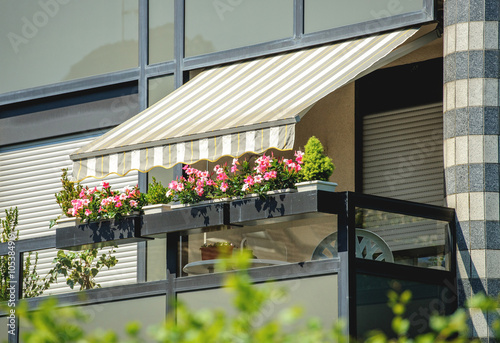 Balcony with awning opened and beautiful flowers - covered by sun-shield on a warm summer day photo