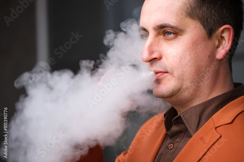 Young man smoking electronic cigarette on background of building