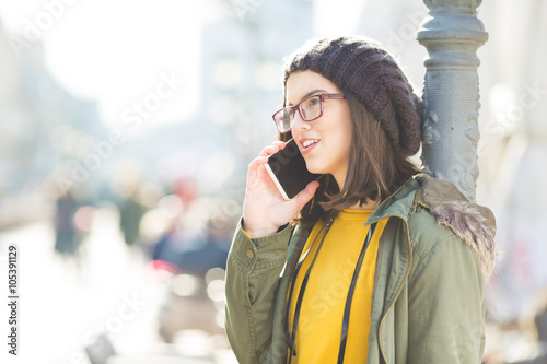 Young modern woman talking on the phone. She is leaning a pillar.