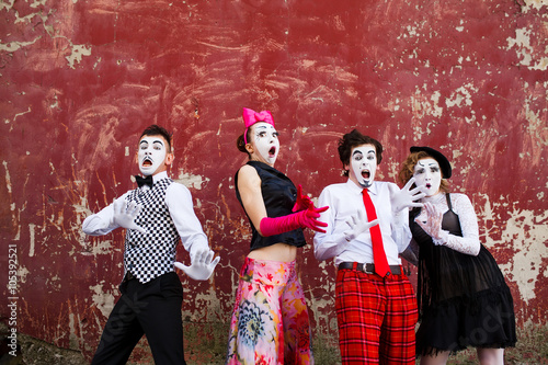 Four mimes in fear stand in the background of a red wall.