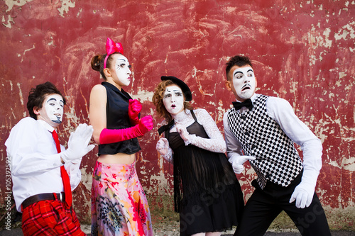 Four mimes standing in awe at the background of a red wall.