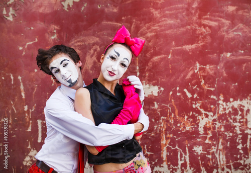 Couple mimes cute pose in front of a red wall.