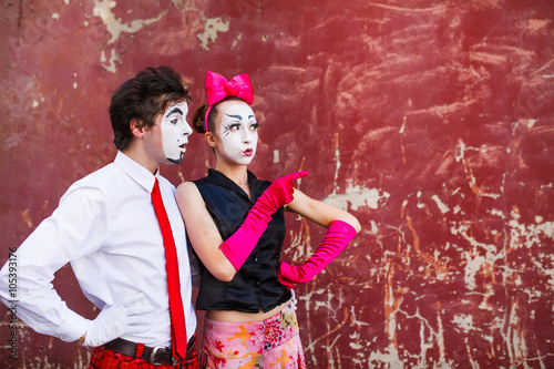 Couple mimes looking aside on the background of a red wall.