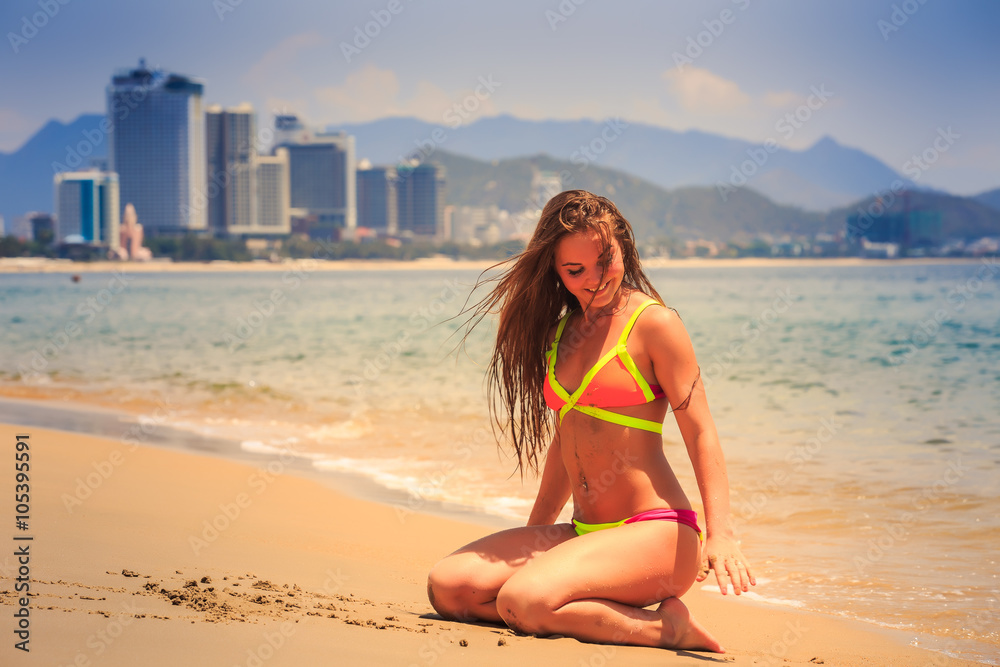 Fototapeta premium blonde slim girl in bikini sits on heels and bottom on wet sand