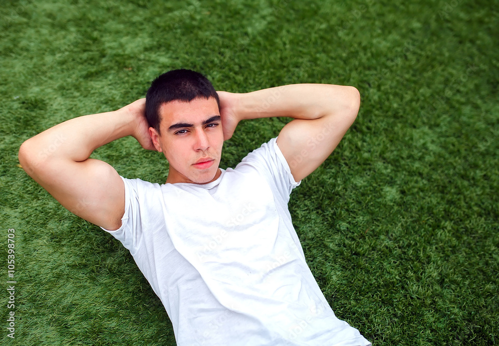 Young man training outdoors and doing sit-ups on green grass. Young man training outdoors and doing sit-ups on green grass.