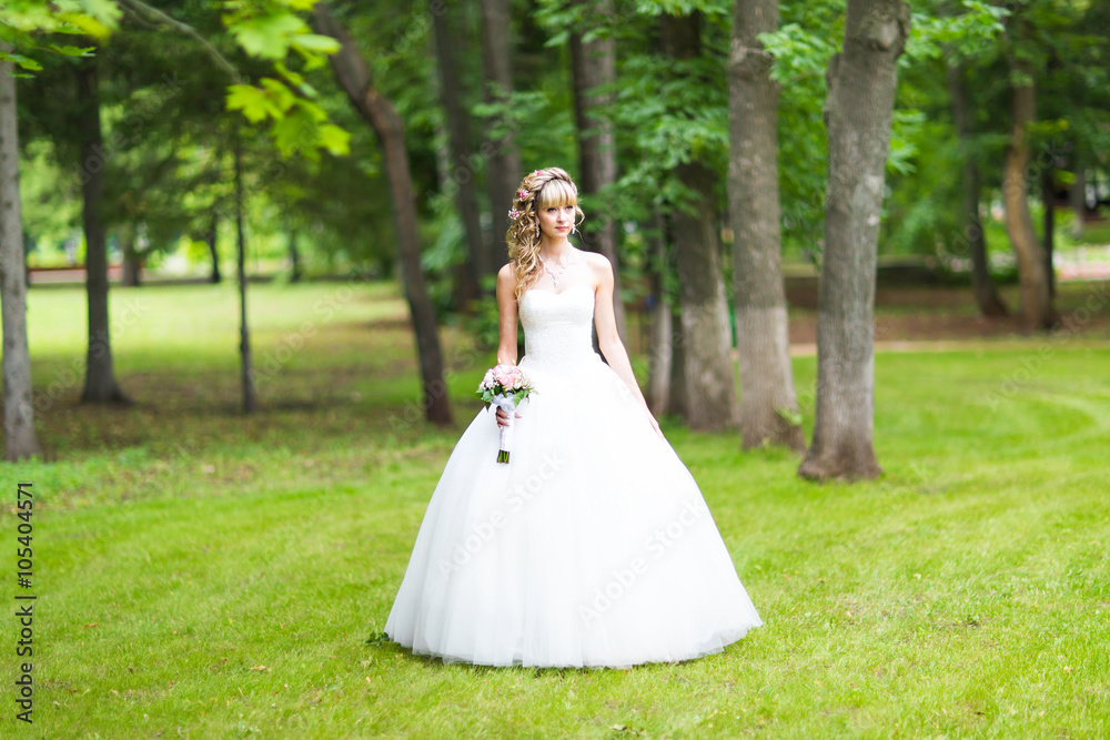 Beautiful bride with wedding bouquet of flowers outdoors in green park.