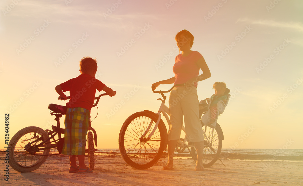 happy mother with two kids biking at sunset