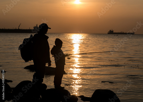 Silhouette of father and daughter fishing with rod at sunset 