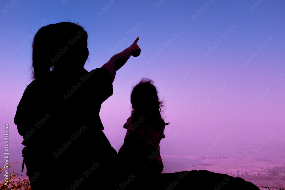 Silhouette back view of mother and child hikers enjoying the view at the top of a mountain. 