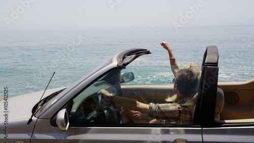 Couple driving convertible together along beach