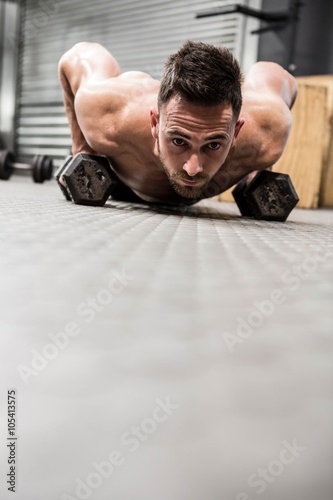 Shirtless man doing push up with dumbbells