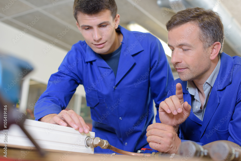 Plumber and appretice with radiator on workbench Plumber and appretice with radiator on workbench