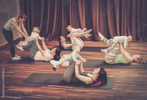 Group of young mothers and their babies doing yoga exercises on rugs at fitness studio.