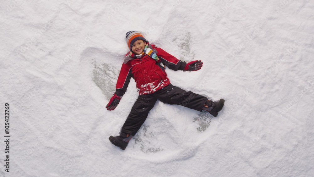 Young boy making snow angel in winter