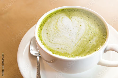 A cup of green tea matcha latte with saucer. Wood table background. Top view.