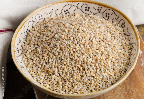 Barley in a ceramic bowl on wooden board.