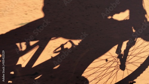 the silhouette of a young man riding a mountain bike on a dirt road