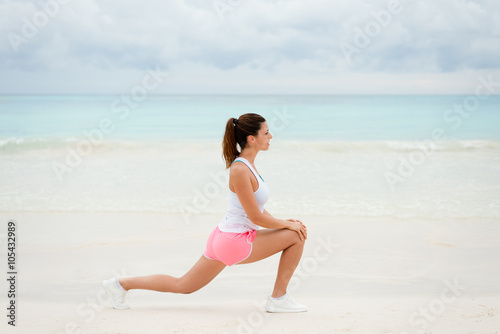 Fitness woman doing stretching legs exercise for warming up before running at the beach. Healthy exercising on summer.