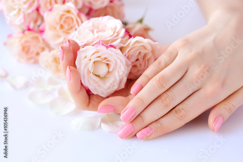 Foto Hands of a woman with pink manicure on nails  and roses against white background