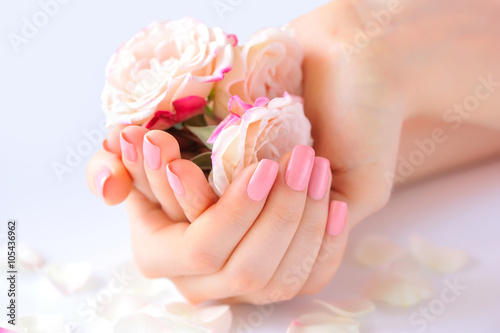 Hands of a woman with pink manicure on nails and roses against white background