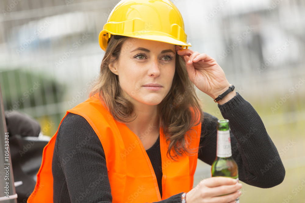 Female architect with safety jacket and helmet drinking beer during working break at construction site