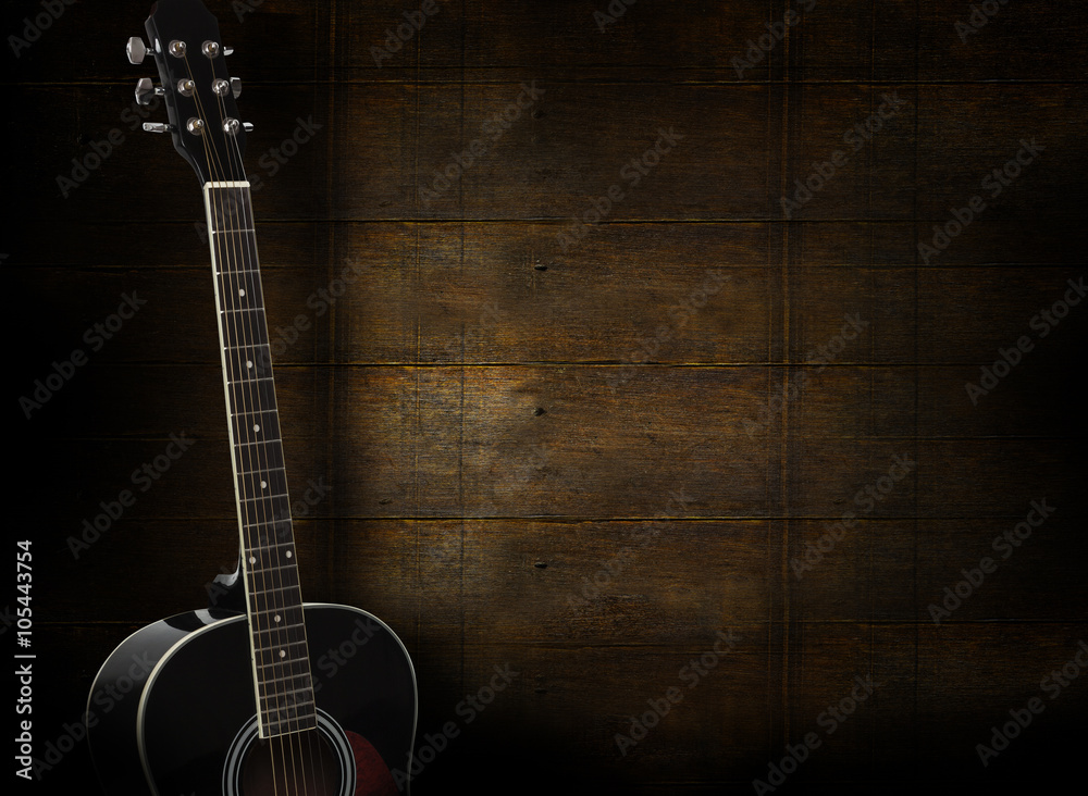 Black acoustic guitar on dark yellow wooden background.