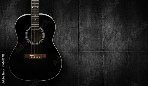 Black acoustic guitar on dark black wooden background.