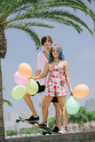 Young couple standing on the skateboard with colorful balloons 
