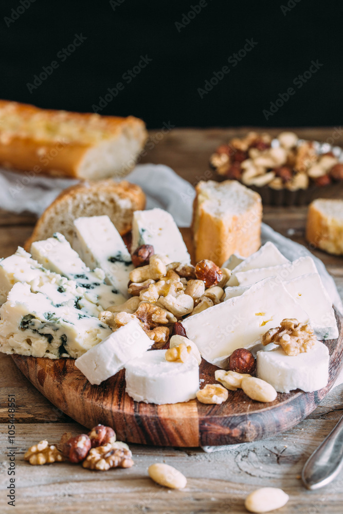 Cheese plate: Emmental, Camembert cheese, blue cheese, bread sticks, walnuts, hazelnuts, honey on wooden table