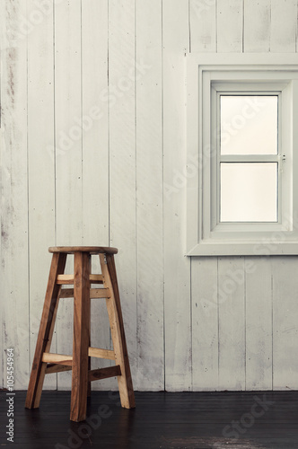 Wooden chair on a dark timber wood floor, near a white windowsill and white wooden wall background.