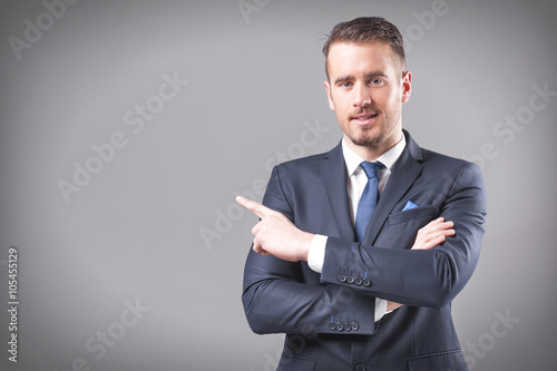 Hnandsome business man pointing at copy space on grey background