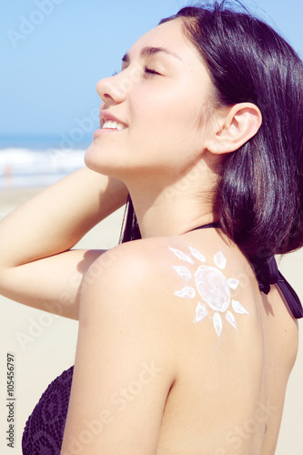 Cute young woman smiling on the beach in bikini with sun painted with cream on the back vertical.