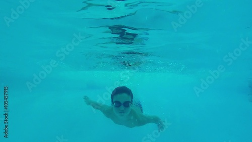 Teen boy swimming underwater in pool.