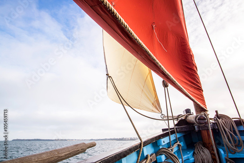 beige cotton jib sail and an ocher sail filled by the wind with wooden mast, bowsprit and hull of an old rigging sailing boat during a sunny sea trip in brittany