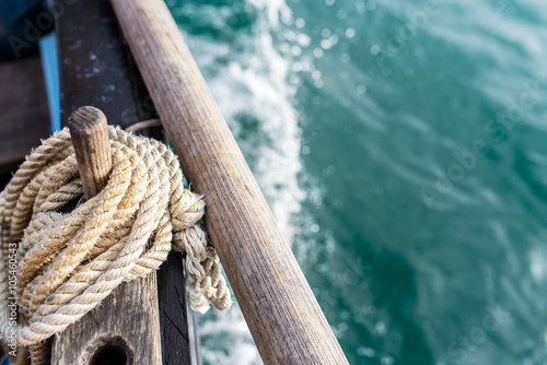 rope wound on a wooden cleat fixed on the hull of a rigging vintage sailing boat with the sea at the blur background during a sunny sea trip in brittany