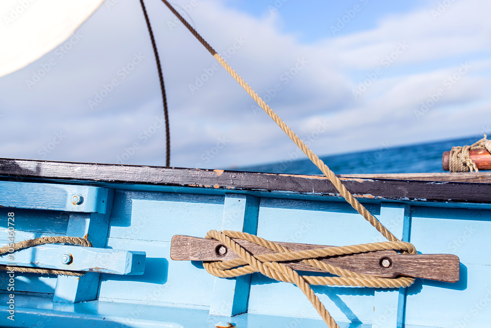 rope of the jib sail wound on a wooden cleat fixed on the blue hull of