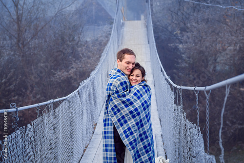 Lovely bride and groom wripped in blanket softly hugs on the wooden bridge. Honeymoon at mountains photo