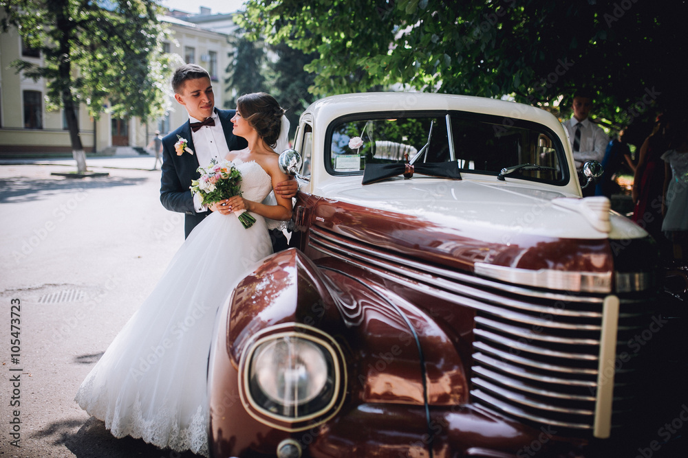 Happy bride and groom hugging and posing near old retro car